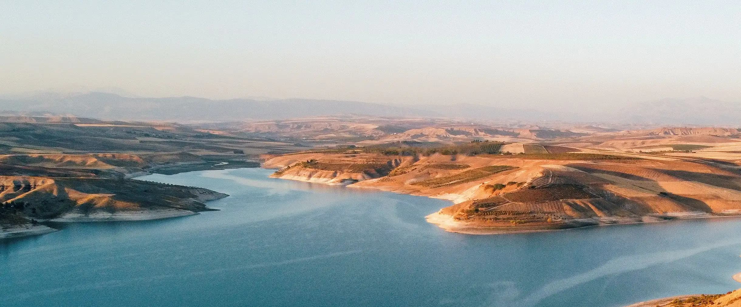 A blue lake winding between golden hills under a clear sky